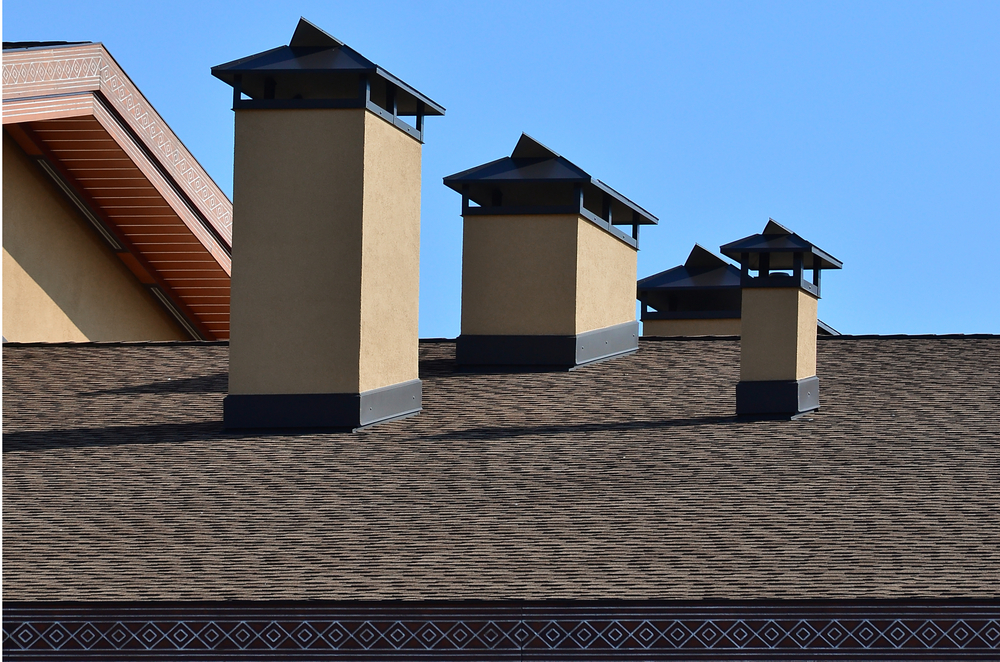 Chimneys with metal flashing installed at the base on an asphalt shingle roof.