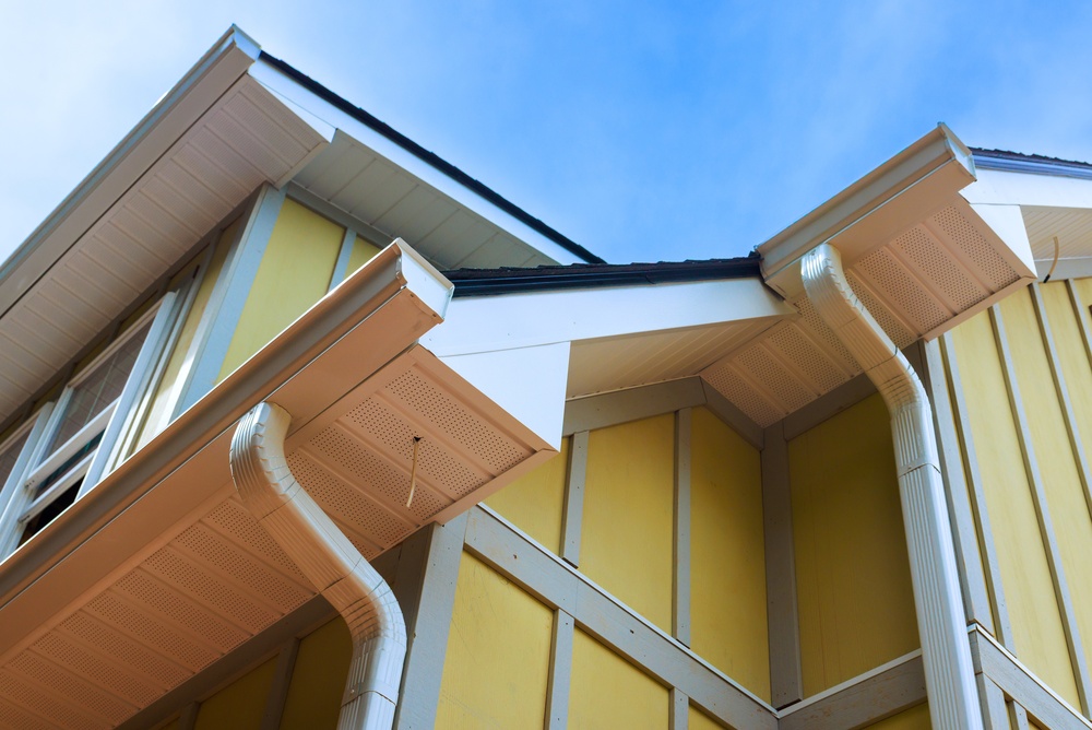 White gutters, downspouts and vented soffits on a two-story home with yellow vertical siding